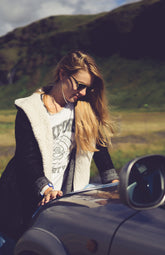 Woman standing next to a car in a scenic outdoor setting with mountains in the background