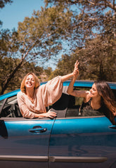 Two women in a blue car with trees in the background